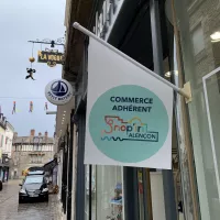 Drapeau de l'association des commerçants "shop'in Alençon" flottant sur la devanture d'un magasin d'habillement.