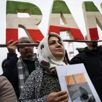 © Nicolas Liponne / Hans Lucas. Lyon, France, 2023-01-08. Une femme porte une pancarte avec une photo devant un logo où il est écrit IRAN lors de la manifestation en soutien au peuple iranien.