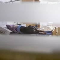 Unite de soins palliatifs a la maison medicale Jeanne Garnier. Patiente allongee sur son lit, vue a travers le hublot ouvert de sa chambre. Paris (75), 6 juin 2018. Photographie de Corinne SIMON / Hans Lucas. 