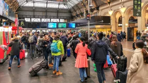 Des voyageurs attendent avec leur bagage et leur valise dans le hall de la gare SNCF Paris Gare de l Est devant des ecrans d information pour les horaires des trains. © Photographie de Nicolas Guyonnet / Hans Lucas