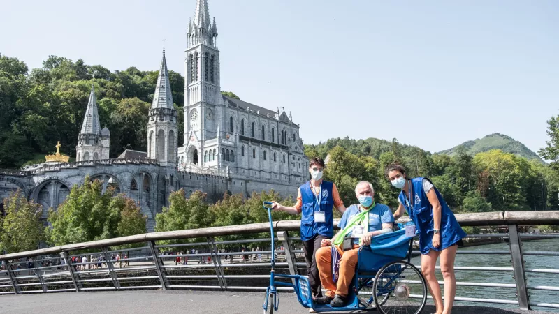 Deux hospitaliers de Lourdes entourent un pèlerin, le 12/08/2021 ©Lilian Cazabet / Hans Lucas