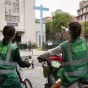 Deux jeunes femmes portant des chasubles au logo "Église verte" à vélo devant la paroisse Saint-Gabriel, Paris, le 16 septembre 2022 ©Corinne Simon / Hans Lucas